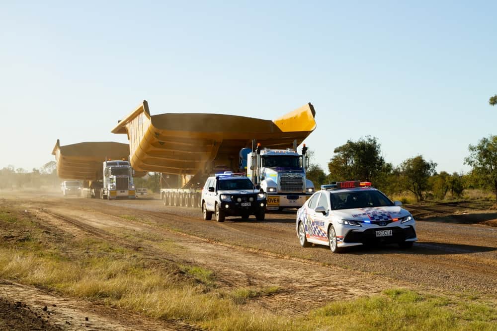 Clermont, Queensland, Australia - August 2022; Two trucks carrying large trays for dump trucks at the Central Queensland coal mines on a dusty unsealed road with traffic control escorts.